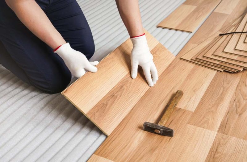 Close-up of a professional installing oak wood flooring with precision, highlighting the alignment process using a rubber mallet.