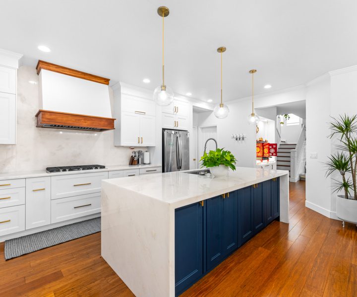 White kitchen with navy island, brass fixtures, and dark hardwood plank flooring