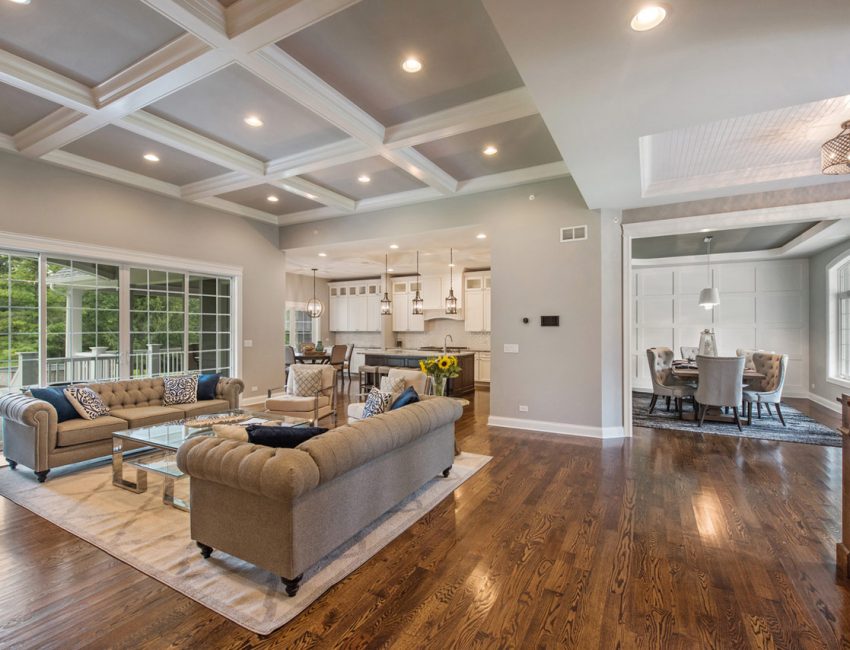 Spacious living room with high-end wood flooring and a meticulously designed ceiling, complemented by natural light and sophisticated furnishings.